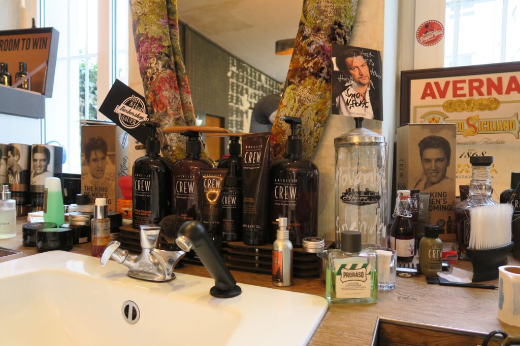 Ein weißes Waschbecken vor einem Spiegel und Haarpflegeprodukten für Männer sowie Bilder von Elvis