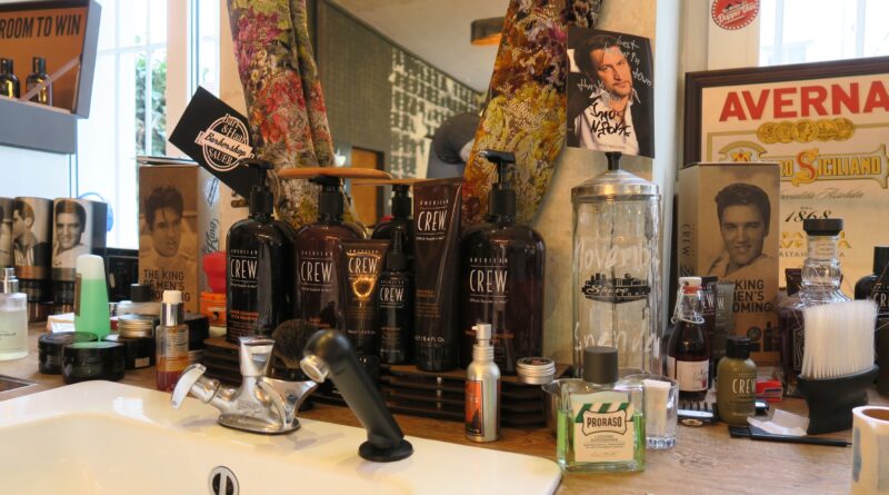 Ein weißes Waschbecken vor einem Spiegel und Haarpflegeprodukten für Männer sowie Bilder von Elvis